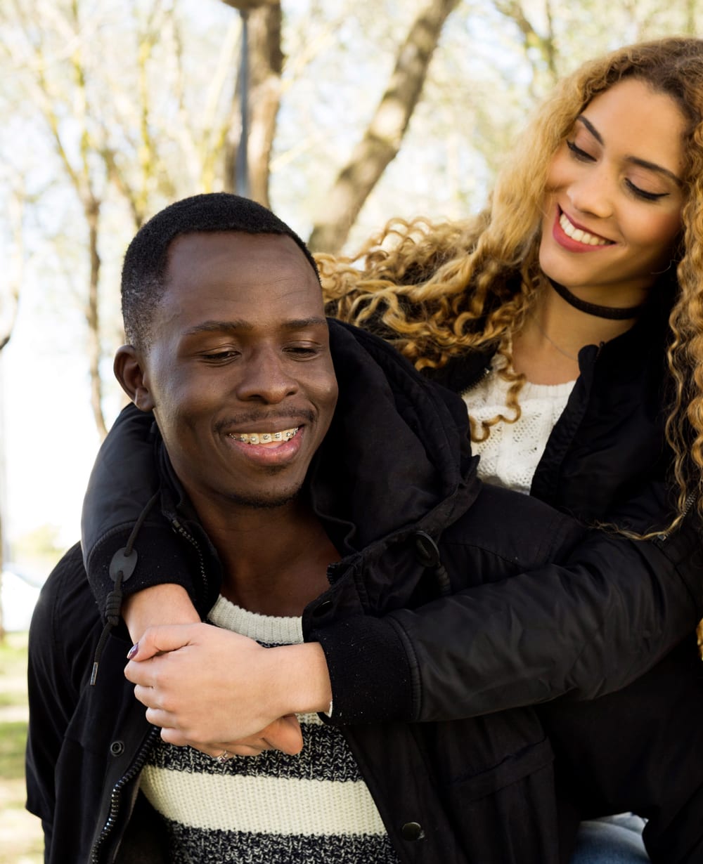 A couple in a park, one giving the other a piggyback, both smiling